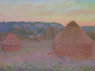 Two large wheat stacks in a field at the end of an autumn day, glowing orange and pink against hills and trees.